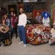 Group of people around a rug tufted vehicle with textiles hanging in the background